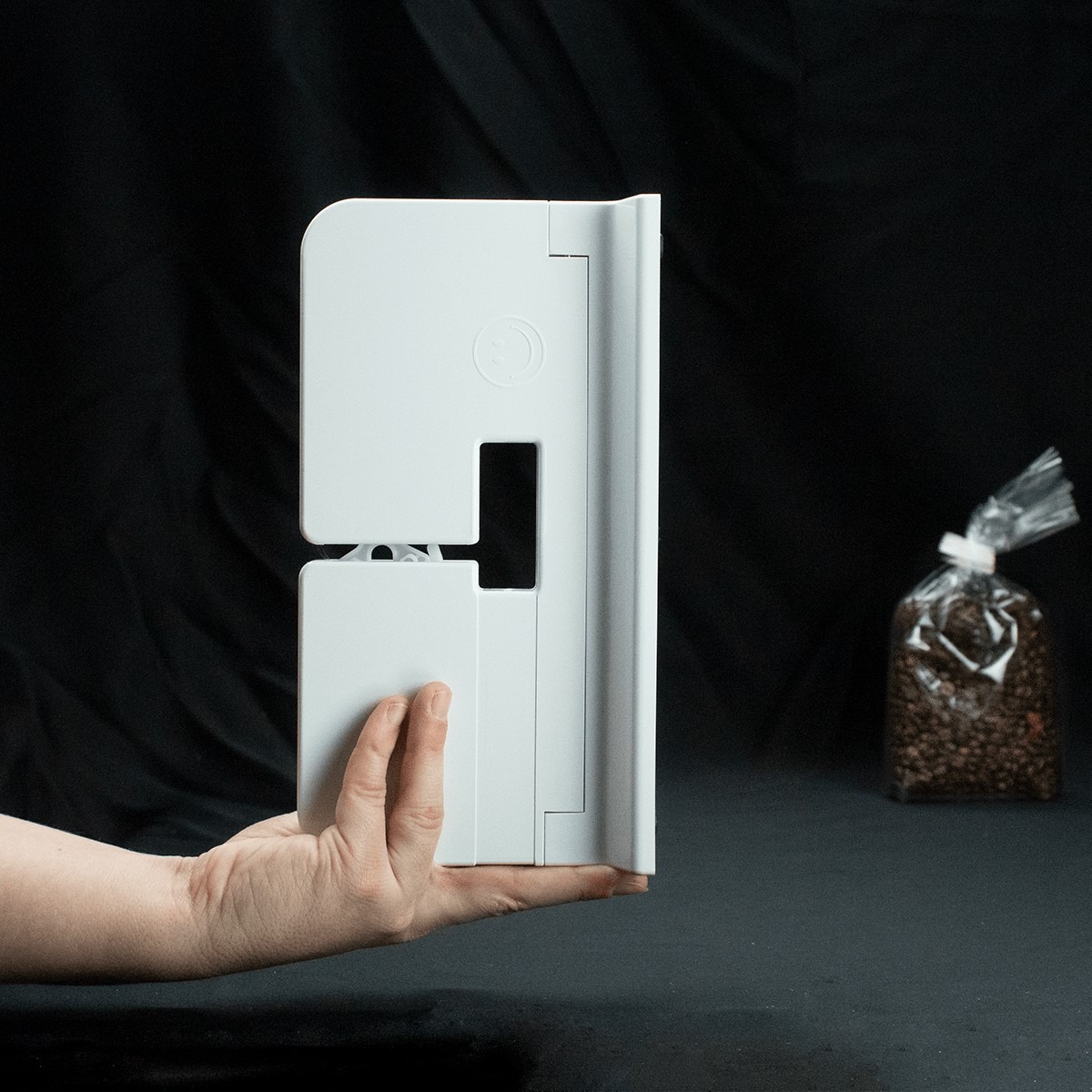The white Innoseal Classic Sealer held in one hand, a sealed bag of coffee beans behind it
